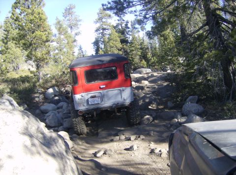 1986 Ford Bronco - An off-road vehicle navigates a challenging rocky path in a wooded area.