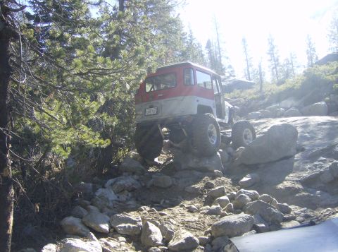 1986 Ford Bronco - An off-road vehicle tackles a challenging rocky trail in a wooded area.