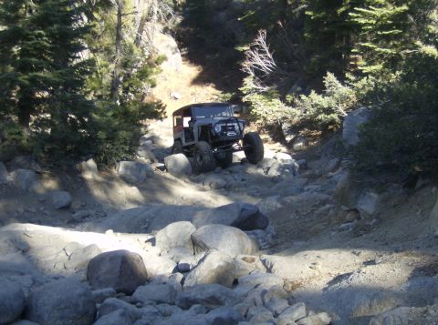 1986 Ford Bronco - An off-road vehicle navigates a challenging, rocky trail through a wooded area.