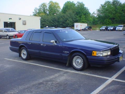 1994 Lincoln Town Car - A blue 1994 Lincoln Town Car is parked in an asphalt lot with a building in the background.