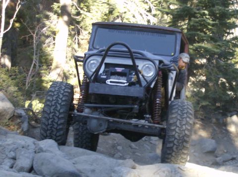 1986 Ford Bronco - This heavily modified off-road vehicle navigates a challenging rocky path through a wooded area.