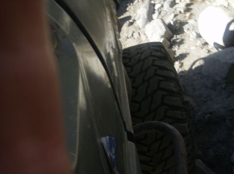 1986 Ford Bronco - View from inside a vehicle shows a large off-road tire and fender against a rocky background.