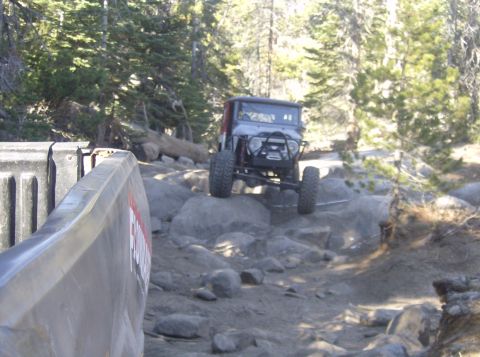 1986 Ford Bronco - An off-road vehicle tackles a challenging rocky path in a wooded area.