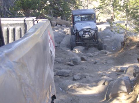 1986 Ford Bronco - An off-road vehicle navigates a challenging rocky path, with the bed of another vehicle visible in the foreground.