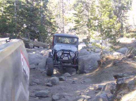 1986 Ford Bronco - Modified off-road vehicle tackling a challenging rocky path in a wooded area.
