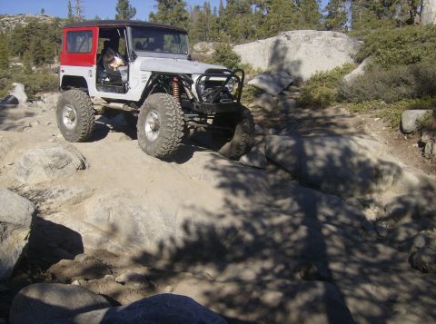 1986 Ford Bronco - This modified off-road vehicle navigates a rocky trail under a clear blue sky.