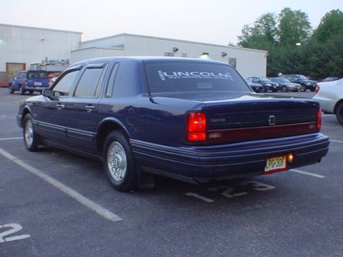 1994 Lincoln Town Car - Rear view of a dark blue Lincoln Town Car with a "LINCOLN" decal on the back window, parked in a lot.