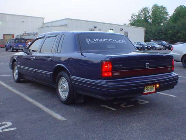Dark blue Lincoln Town Car rear 3/4 view parked in a lot with LINCOLN rear window banner