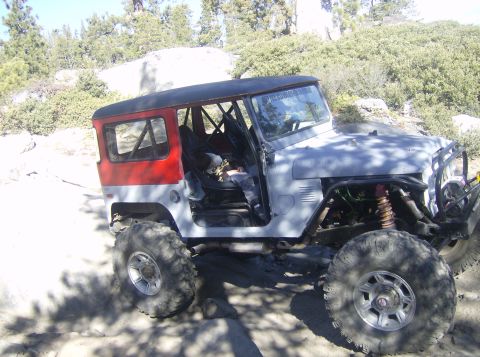 1986 Ford Bronco - This modified off-road vehicle features a two-tone paint scheme with red rear panels and a black roof, equipped for terrain.