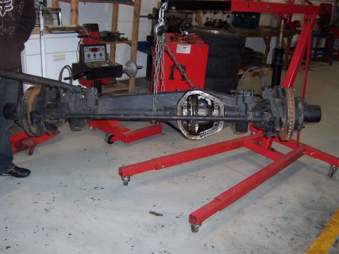 1990 Ford Bronco - Front axle assembly, likely Dana 60, is suspended and supported by a red stand in a workshop.