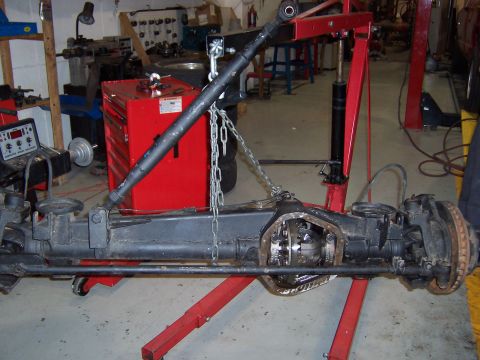 1990 Ford Bronco - The front axle assembly is suspended by chains and an engine hoist, with a red toolbox in the background.