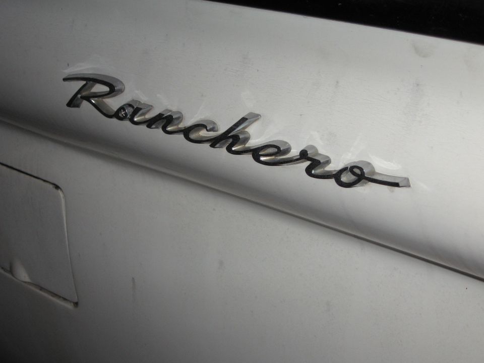 Close-up of a 'Ranchero' emblem on a silver vehicle. The emblem is in script font