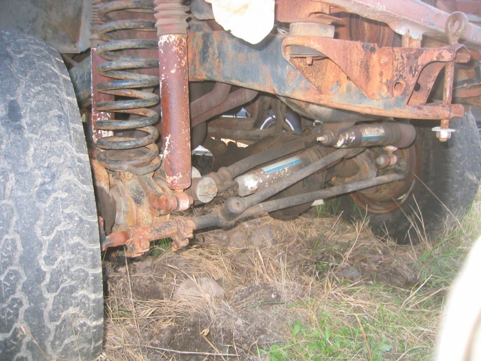 Rusty coil-spring front suspension with radius arm and dual blue shocks under truck