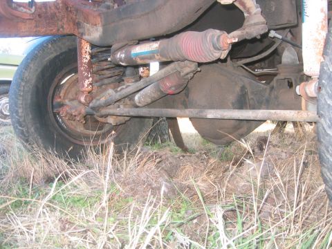 1973 Ford F-100 - Ground-level look under a truck's front end at a rusty solid axle with cast differential housing, coil spring, twin shocks with red boots,…