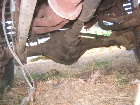 1973 Ford F-100 - Underbody view looking up at a solid front axle housing with cast center section, drag link and tie rod ends, coil spring and radius arm, p…