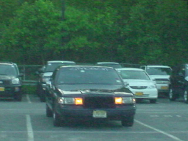 Black sedan parked in a lot, front view, amber turn signals illuminated