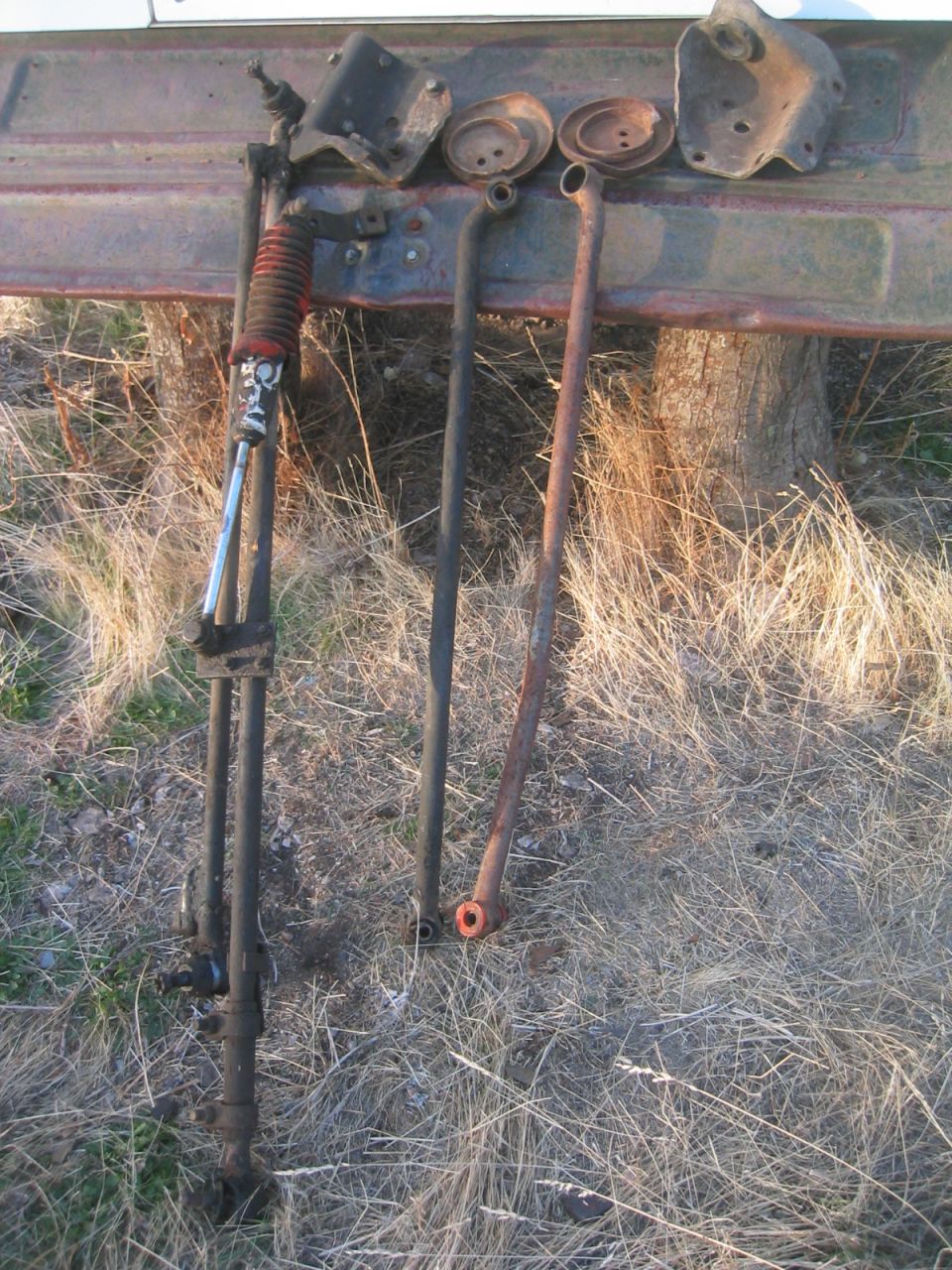 Rusty radius arms, coil spring seats and brackets leaned against a truck bed outdoors