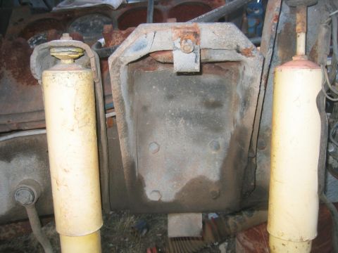 1973 Ford F-100 - Two weathered yellow-bodied shock absorbers stand upright on either side of a rusty stamped-steel spring/shock tower bracket, one shock sti…