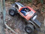 1992 Ford Mustang - An off-road RC car navigates a wooded trail with large, knobby tires.