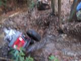 1992 Ford Mustang - An off-road vehicle lies on its side amidst trees and debris, with another vehicle partially visible behind it.