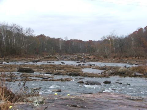 1996 Ford Bronco - A wide shot of a rocky riverbed with rapids and trees lining the banks under a cloudy sky.