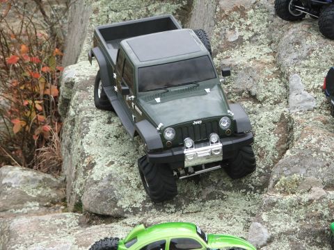 1996 Ford Bronco - A green Jeep pickup truck navigates a rocky terrain, with another vehicle visible below.