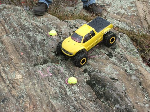 1996 Ford Bronco - RC monster truck positioned on a rocky surface with tennis balls scattered around.
