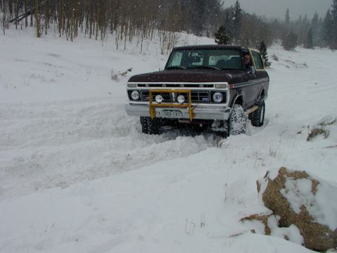 1979 Ford Bronco - A maroon Ford Bronco navigates a snowy terrain, its front bull bar equipped with lights.