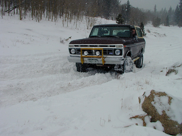 Maroon Ford Bronco driving in snow, front bull bar with lights, snow-covered tires