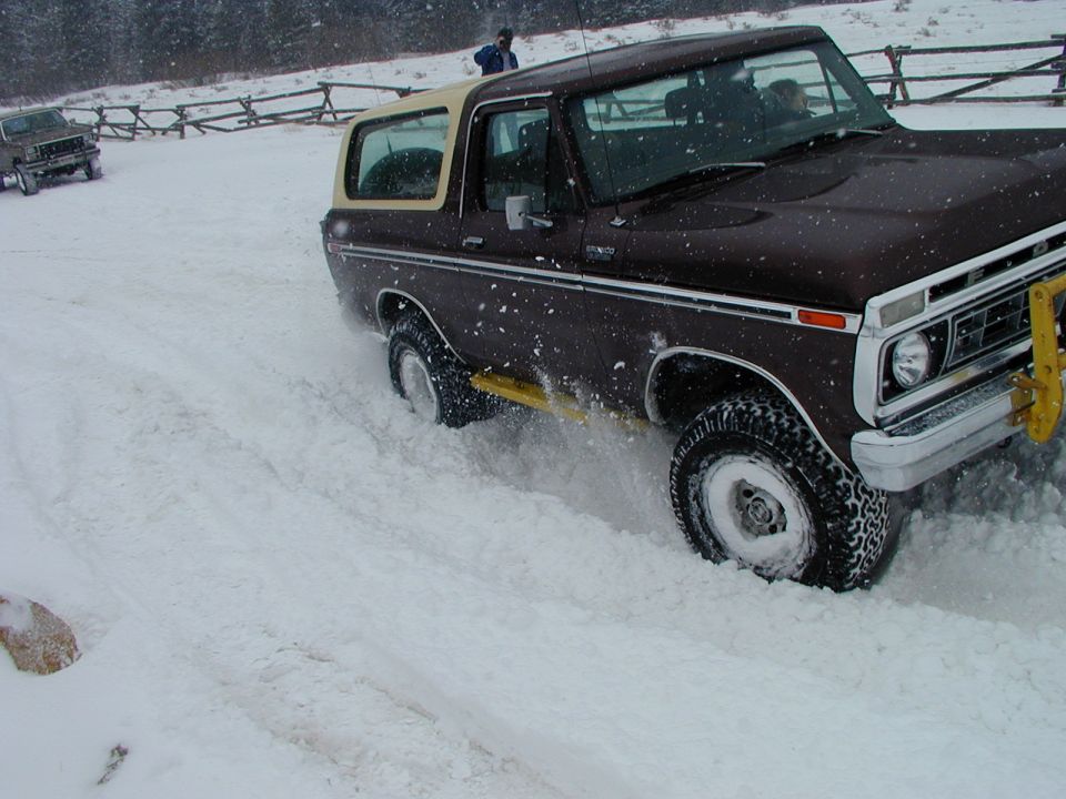 Brown Bronco with tan top driving in snow, another vehicle behind it