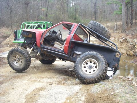 1978 Ford Bronco - Two heavily modified off-road vehicles are seen navigating a muddy trail with water obstacles.
