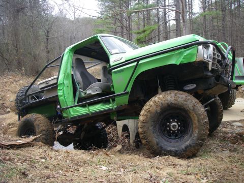 1978 Ford Bronco - A modified green off-road vehicle navigates a muddy terrain with its tires partially submerged.