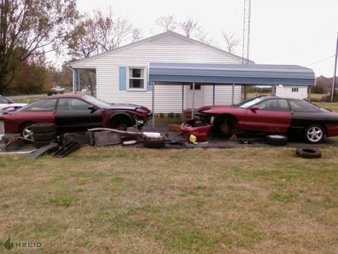 1993 Ford Probe - Two Ford Probes, one with its front end disassembled, sit in a yard next to a house.