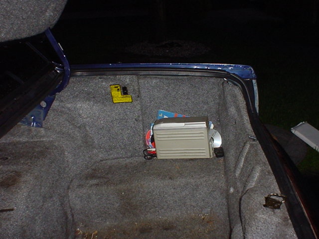 Open trunk of a dark blue sedan with a silver electronic module mounted on gray carpet