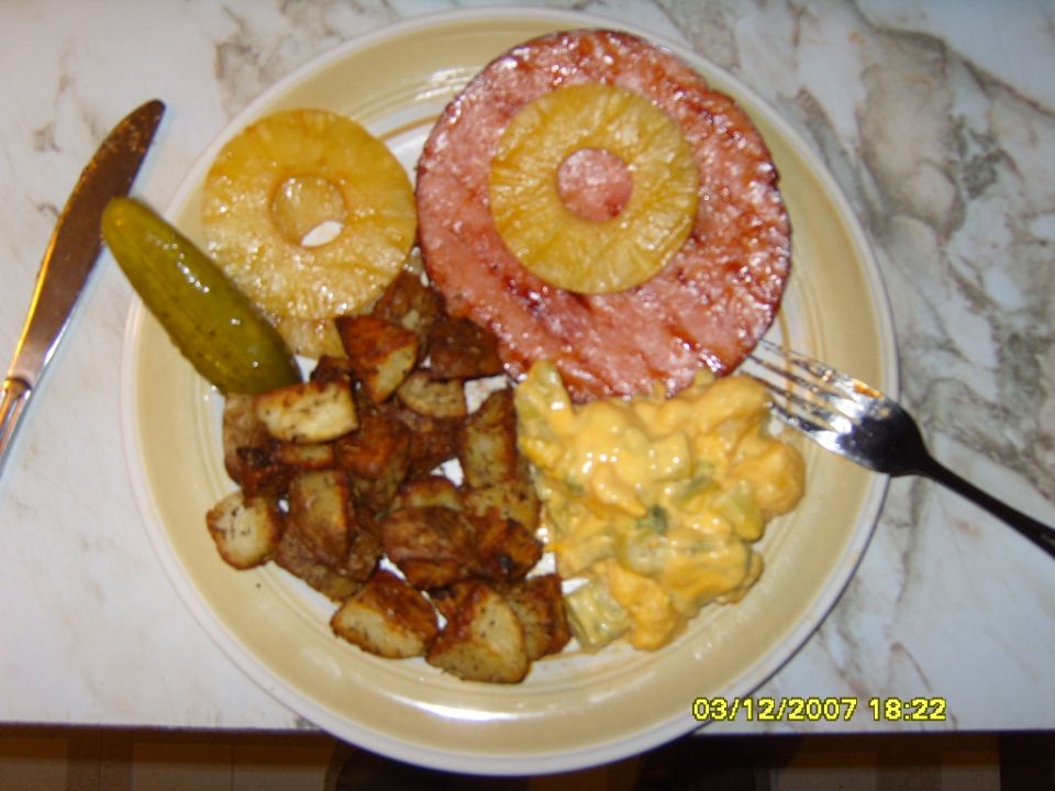 Plate of ham, pineapple rings, fried potatoes, pickle, and macaroni salad