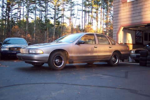 2001 Ford Crown Victoria - A tan Chevrolet Caprice is parked outside a garage, with another car visible in the background.