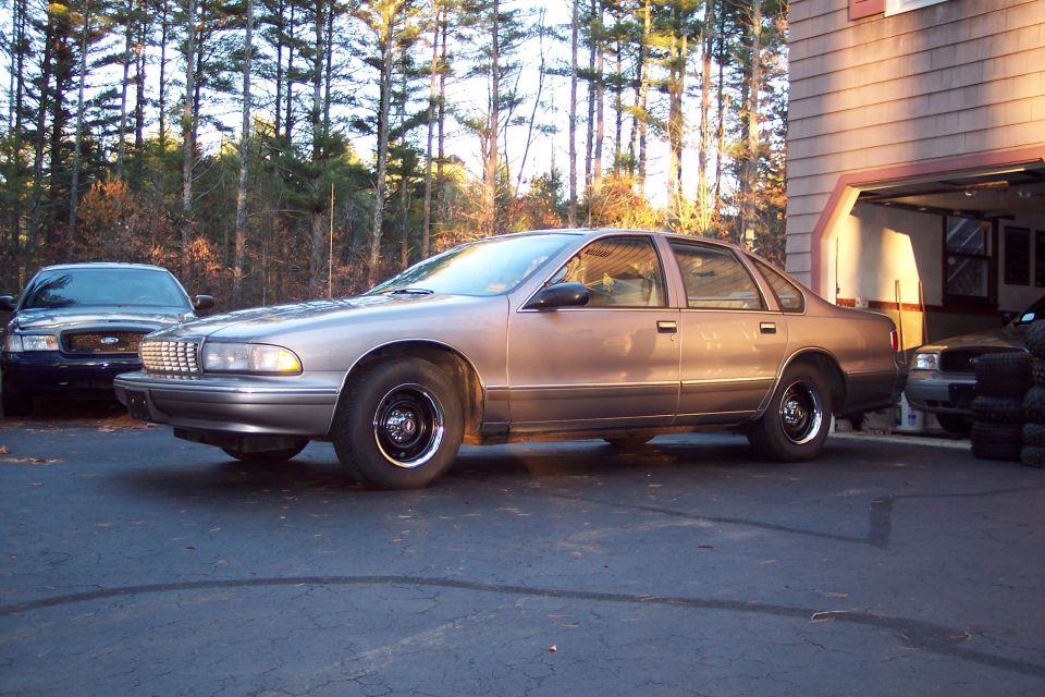 Side view of a tan 1996 Chevrolet Caprice parked in a driveway, with a dark sedan in the background