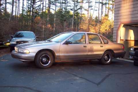 2001 Ford Crown Victoria - A tan 1995 Chevrolet Caprice sedan is parked on an asphalt driveway next to a garage, with trees in the background.