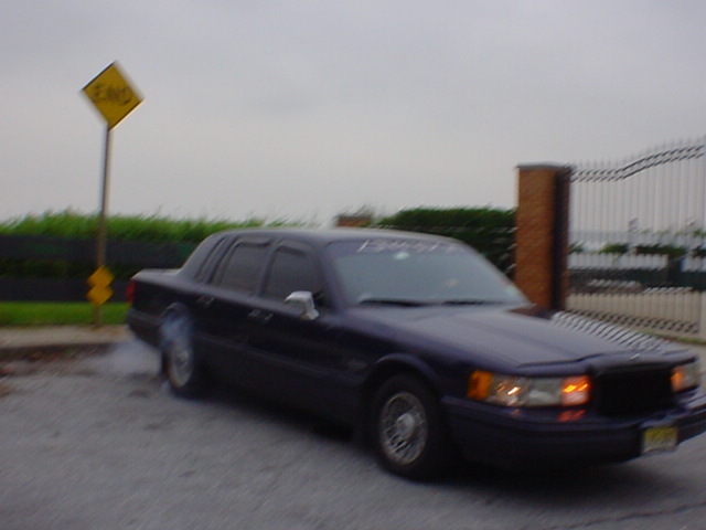 Dark sedan with a vinyl banner on the windshield, seen from the front-right