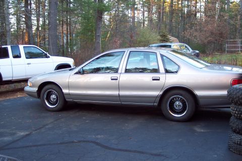 2001 Ford Crown Victoria - A silver 1995 Chevrolet Caprice sedan is parked next to a white pickup truck, with trees in the background.