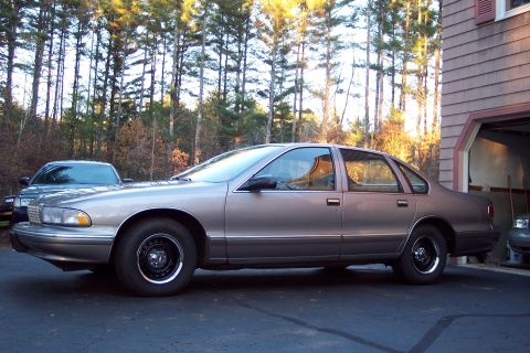 2001 Ford Crown Victoria - A 1990s Chevrolet Caprice sedan is parked outside a garage, with another car partially visible inside.