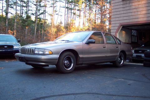 2001 Ford Crown Victoria - A brown Chevrolet Caprice is parked in a driveway next to a garage containing another vehicle.
