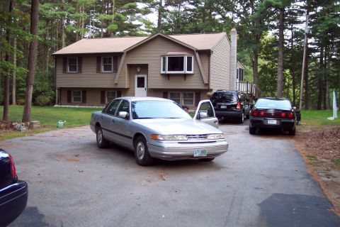 2001 Ford Crown Victoria - A silver 2001 Ford Crown Victoria is parked in the driveway of a suburban home, with other vehicles present.