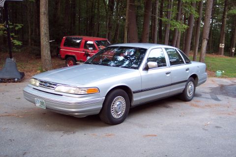 2001 Ford Crown Victoria - A silver 2001 Ford Crown Victoria is parked in a driveway with trees and a red SUV behind it.