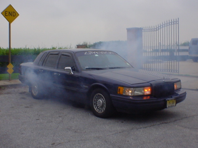1994 Lincoln Town Car doing a burnout, smoke coming from tires. Yellow 'END' sign visible