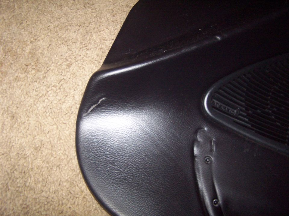 Black car door panel interior with speaker grille and visible damage. Text 'TREBLE' visible on speaker cover
