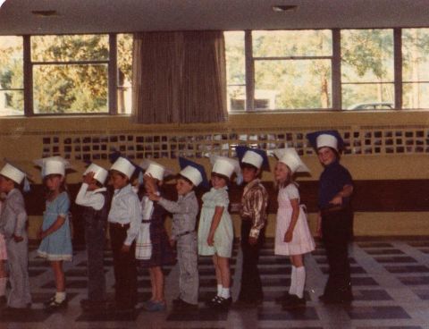 2000 Ford Crown Victoria - A group of children dressed in graduation caps stand in a line indoors.