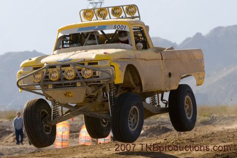 1996 Ford Bronco - This heavily modified truck is airborne during a desert race, kicking up dust.