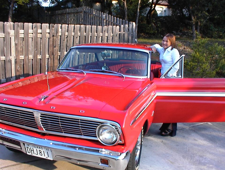 Red Ford convertible front 3/4 view with woman standing by open door, Texas plate DHJ 811