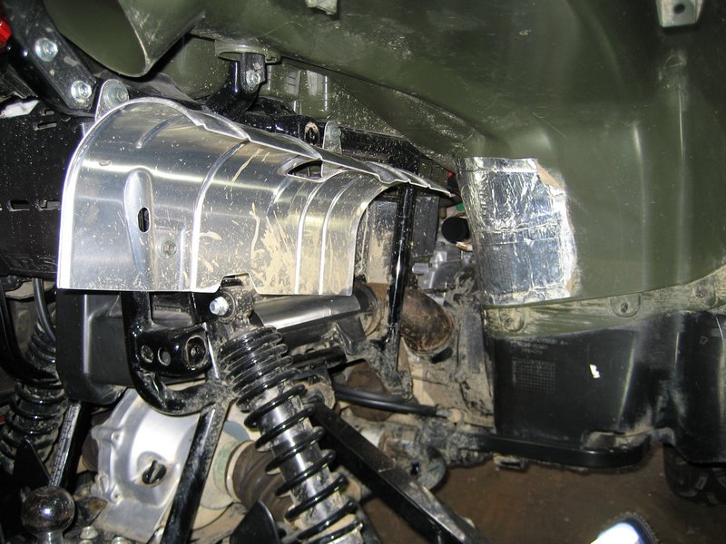 Chrome heat shield and coil-over shock in ATV engine bay with green body panels